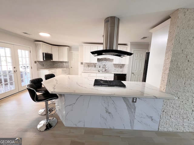 kitchen with french doors, light stone countertops, island range hood, white cabinetry, and a breakfast bar area