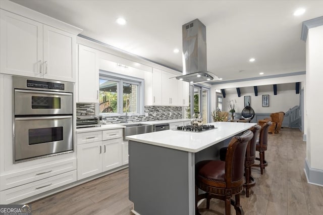 kitchen with island range hood, a kitchen island, white cabinets, and appliances with stainless steel finishes