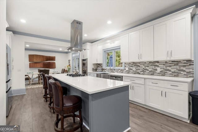 kitchen with a breakfast bar, white cabinetry, island range hood, a center island, and ornamental molding