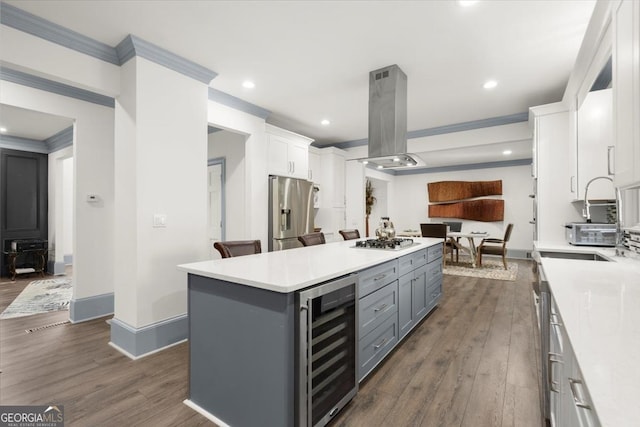 kitchen with appliances with stainless steel finishes, a kitchen island, white cabinets, beverage cooler, and island exhaust hood