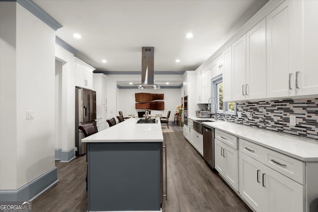 kitchen with sink, appliances with stainless steel finishes, island exhaust hood, white cabinets, and a kitchen island