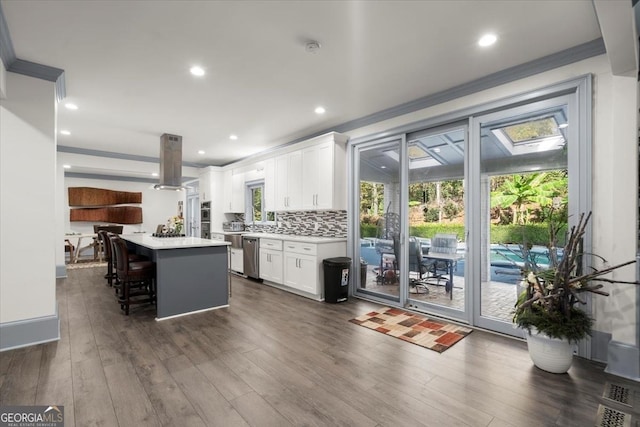 kitchen with a kitchen island, island range hood, white cabinets, a kitchen breakfast bar, and decorative backsplash