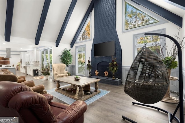 living room featuring beamed ceiling, light wood-type flooring, a fireplace, and high vaulted ceiling