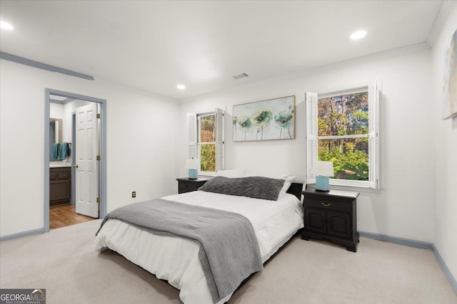 bedroom with multiple windows, light carpet, and ensuite bathroom