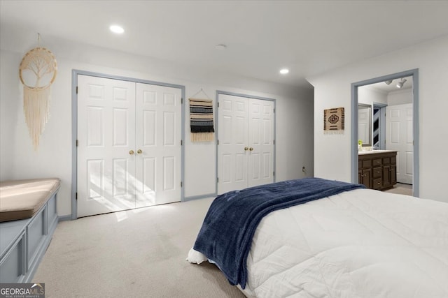 bedroom with light carpet, two closets, and ensuite bath