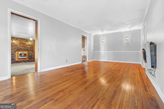 unfurnished living room featuring a brick fireplace, ornamental molding, heating unit, and wood-type flooring