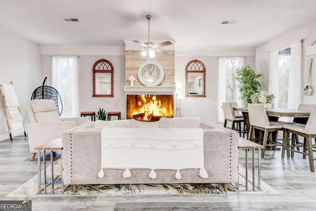 living room featuring a fireplace, light hardwood / wood-style floors, crown molding, and a healthy amount of sunlight