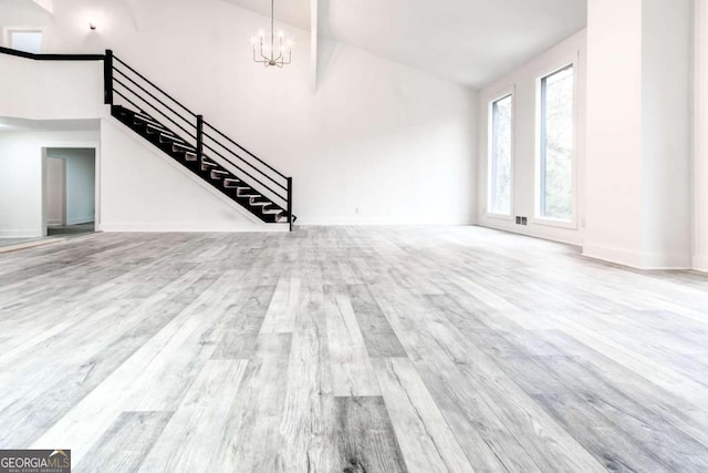 unfurnished living room featuring light wood-type flooring, a towering ceiling, and a notable chandelier