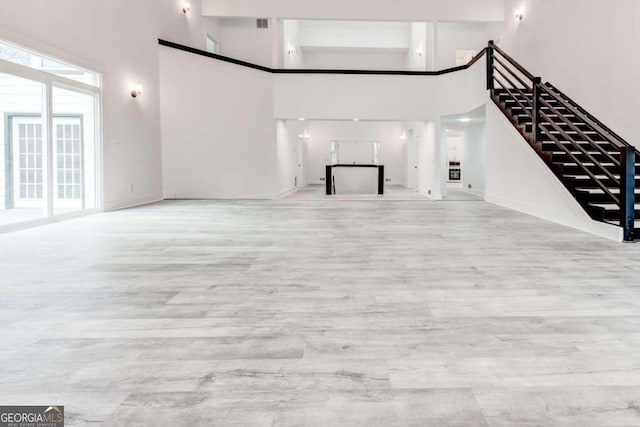 unfurnished living room with light hardwood / wood-style floors and a towering ceiling