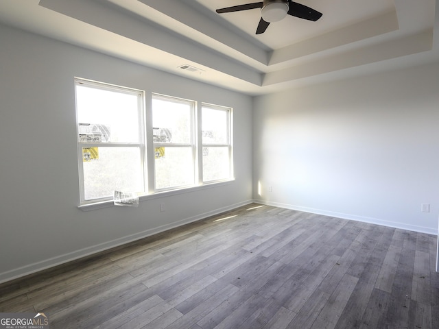 spare room with baseboards, visible vents, a tray ceiling, and wood finished floors