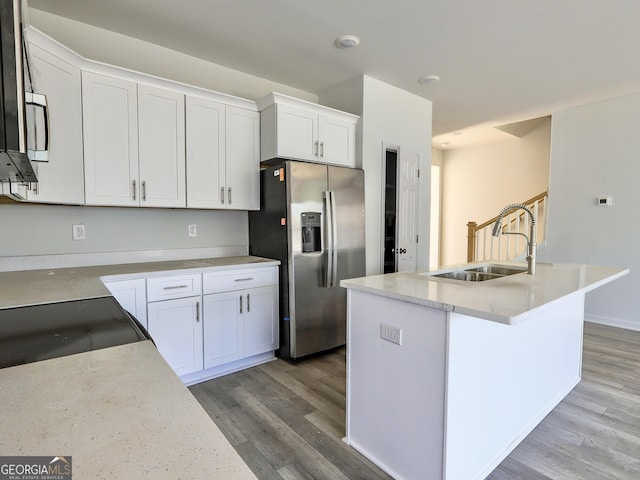 kitchen featuring a sink, an island with sink, stainless steel fridge, and white cabinetry