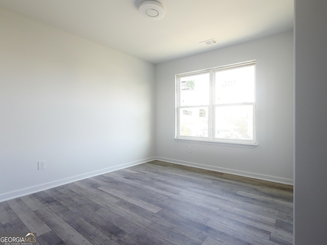 empty room featuring wood finished floors, visible vents, and baseboards