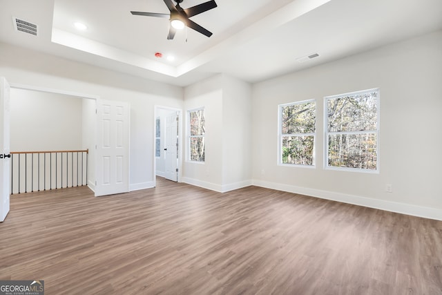 empty room featuring a tray ceiling, ceiling fan, and hardwood / wood-style floors