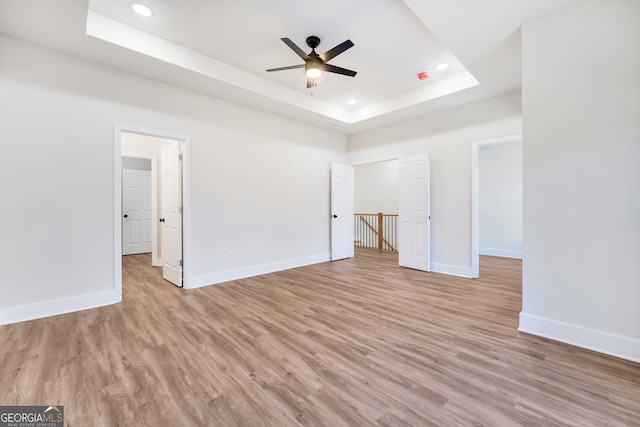 unfurnished bedroom featuring a raised ceiling, ceiling fan, and light hardwood / wood-style flooring