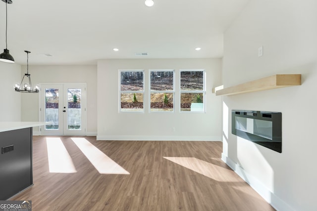 unfurnished living room with light hardwood / wood-style flooring, a chandelier, and french doors