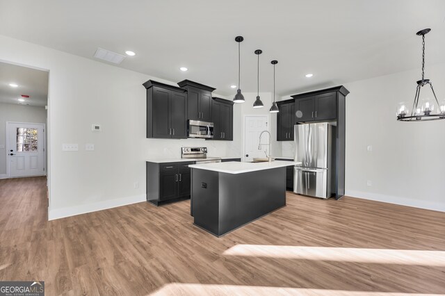 kitchen featuring decorative light fixtures, light wood-type flooring, an island with sink, appliances with stainless steel finishes, and a notable chandelier