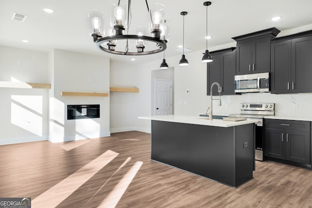 kitchen with an inviting chandelier, hardwood / wood-style flooring, an island with sink, decorative light fixtures, and stainless steel appliances