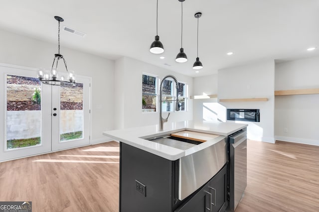 kitchen with hanging light fixtures, light hardwood / wood-style flooring, a kitchen island with sink, and stainless steel dishwasher