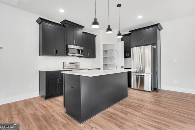 kitchen with pendant lighting, a kitchen island with sink, light hardwood / wood-style flooring, decorative backsplash, and appliances with stainless steel finishes