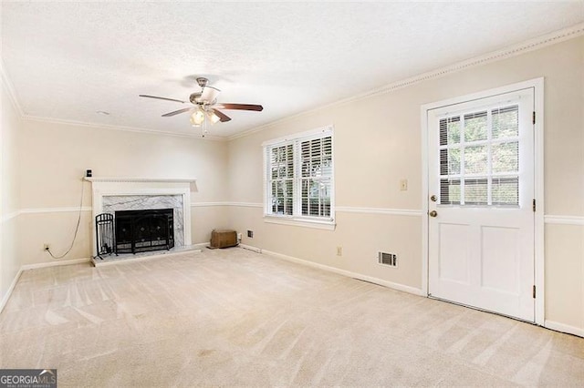 unfurnished living room featuring ceiling fan, crown molding, light colored carpet, a textured ceiling, and a fireplace