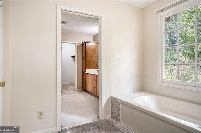 bathroom featuring vanity, a bath, a textured ceiling, and a wealth of natural light