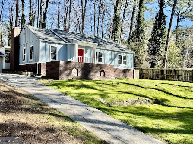 view of front of house with brick siding, a chimney, board and batten siding, a front yard, and fence