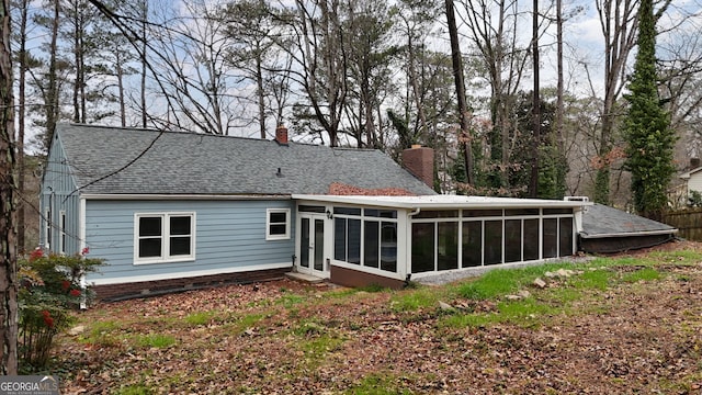 back of property with a shingled roof, a chimney, and a sunroom