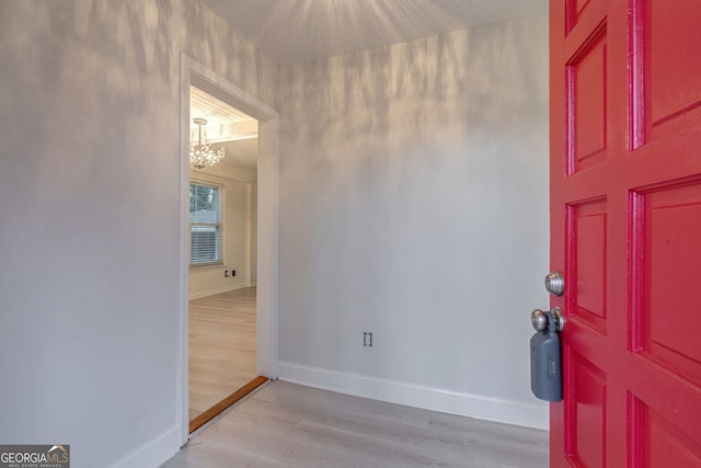 entryway with baseboards, a chandelier, and light wood finished floors