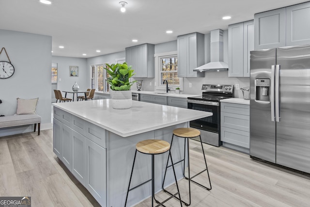 kitchen featuring gray cabinetry, stainless steel appliances, wall chimney range hood, light hardwood / wood-style flooring, and a kitchen island