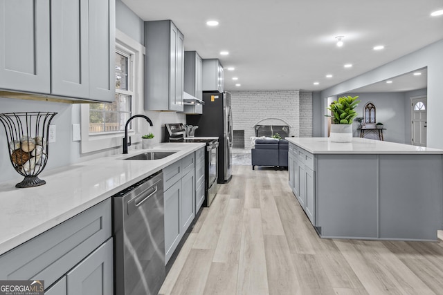 kitchen featuring appliances with stainless steel finishes, a brick fireplace, light hardwood / wood-style floors, sink, and gray cabinets