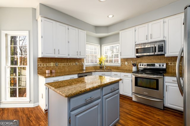 kitchen with dark wood-type flooring, dark stone countertops, appliances with stainless steel finishes, a kitchen island, and white cabinetry