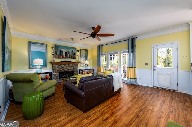 living room featuring dark hardwood / wood-style floors, ceiling fan, a stone fireplace, and crown molding