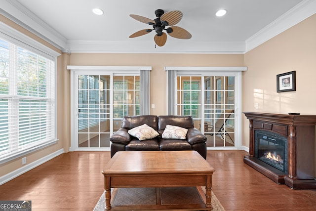 living room with a glass covered fireplace, crown molding, baseboards, and wood finished floors