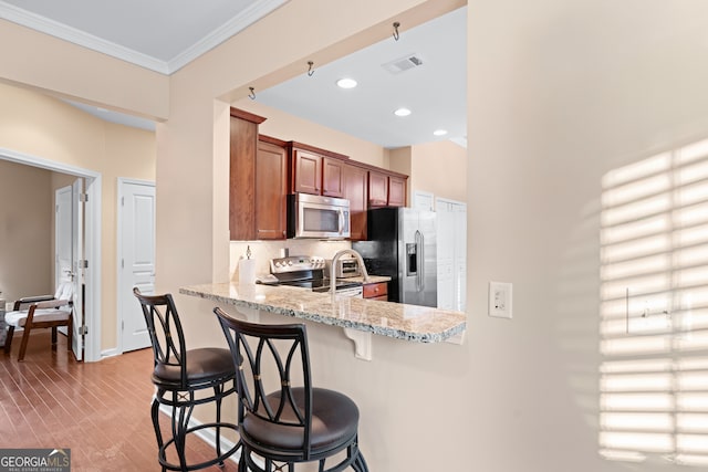 kitchen with visible vents, ornamental molding, stainless steel appliances, a breakfast bar area, and light stone countertops