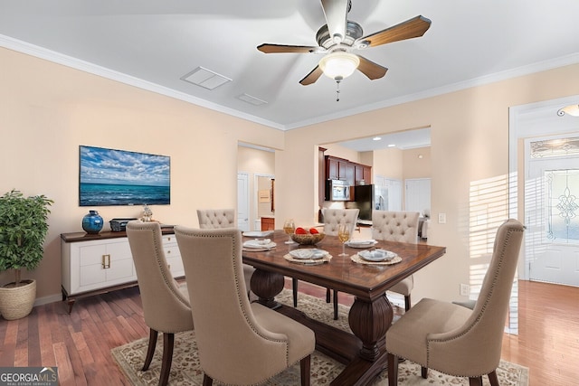 dining space featuring hardwood / wood-style floors, baseboards, visible vents, ceiling fan, and ornamental molding