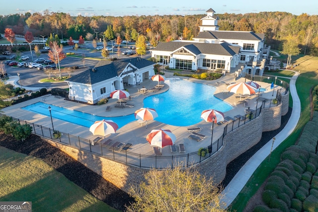 community pool with a patio, fence, and a forest view