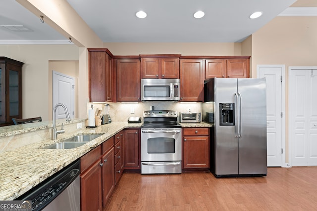 kitchen with light stone counters, light wood-style flooring, a sink, appliances with stainless steel finishes, and tasteful backsplash