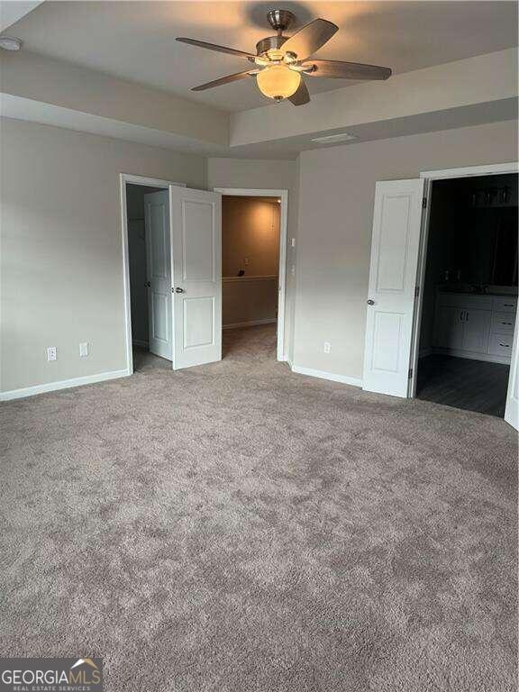 unfurnished bedroom with carpet, a walk in closet, ensuite bathroom, and ceiling fan