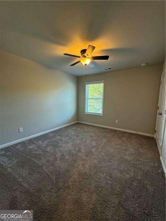 spare room with dark colored carpet and ceiling fan