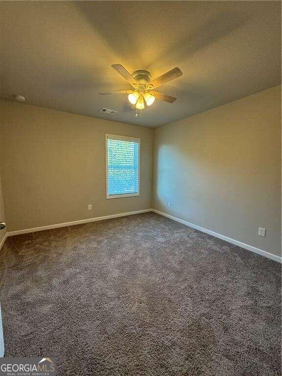 spare room featuring dark carpet and ceiling fan