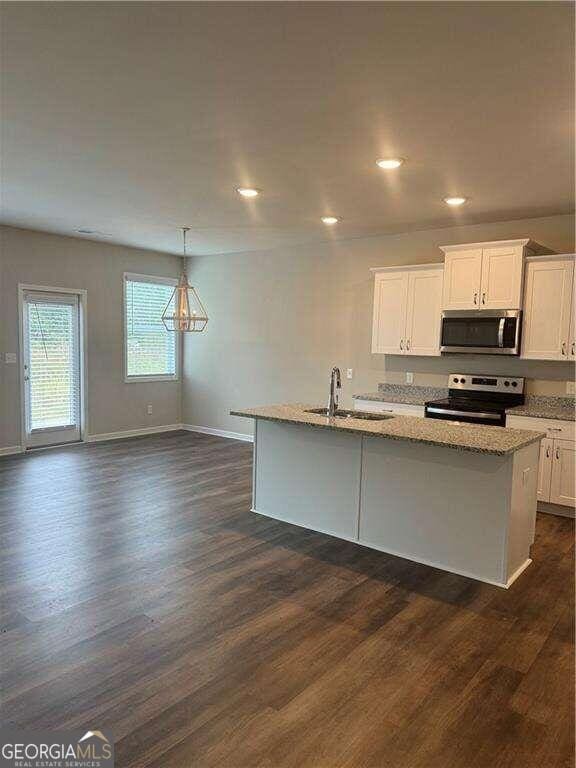 kitchen with light stone countertops, stainless steel appliances, sink, white cabinets, and dark hardwood / wood-style floors