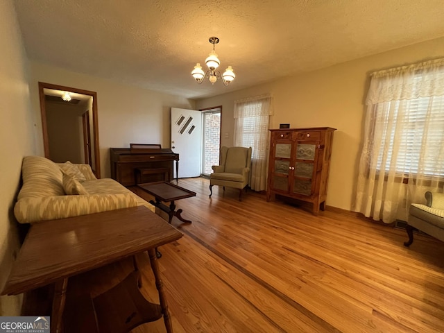 living area featuring a notable chandelier, a healthy amount of sunlight, light hardwood / wood-style flooring, and a textured ceiling