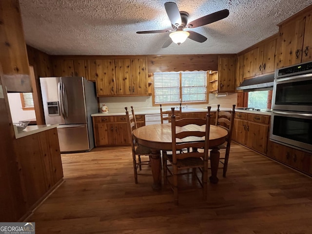 kitchen with ceiling fan, stainless steel appliances, wooden walls, and light hardwood / wood-style flooring