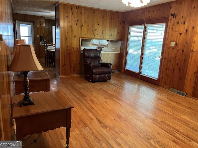 living room with wooden walls, a textured ceiling, and light wood-type flooring