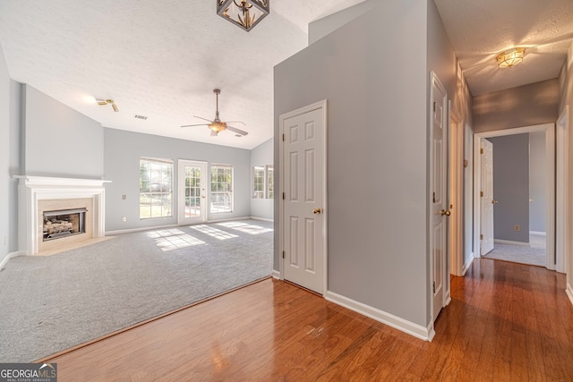 unfurnished living room with hardwood / wood-style floors, a textured ceiling, vaulted ceiling, and ceiling fan