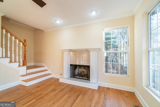 unfurnished living room featuring wood-type flooring, ornamental molding, and a tiled fireplace