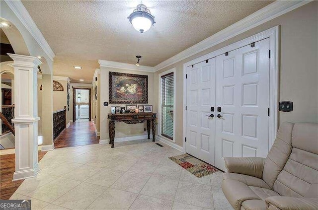 foyer entrance with a textured ceiling, decorative columns, light hardwood / wood-style flooring, and ornamental molding