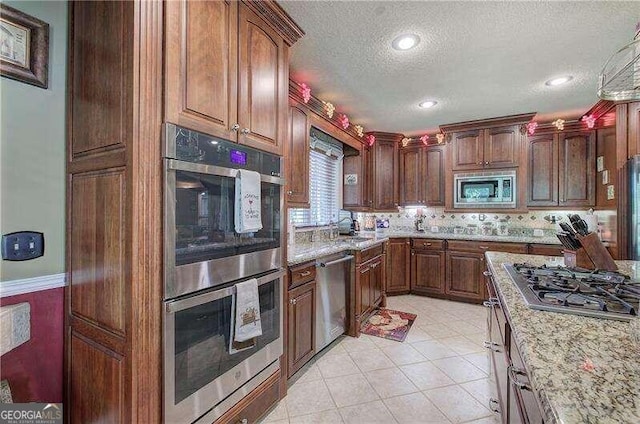 kitchen with light stone countertops, stainless steel appliances, tasteful backsplash, a textured ceiling, and light tile patterned flooring