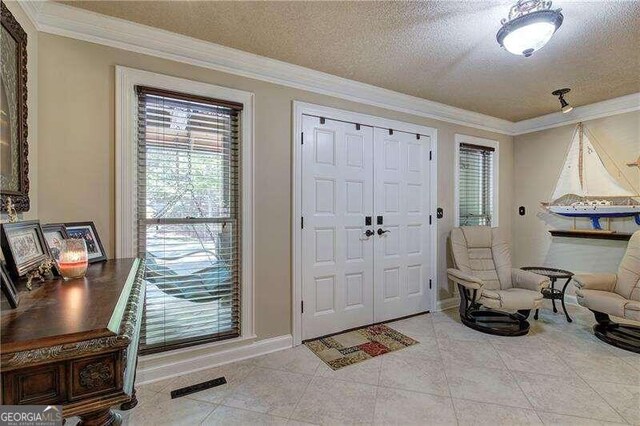 entryway featuring crown molding, light tile patterned floors, and a textured ceiling