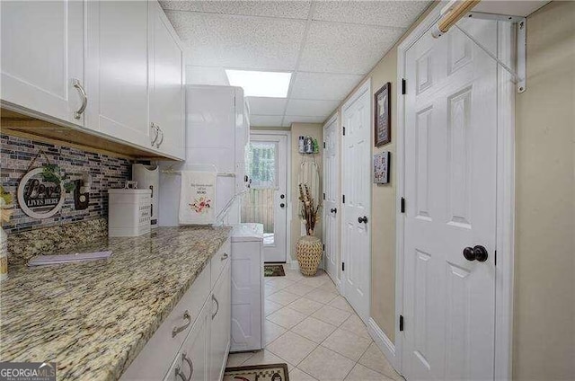 kitchen with white cabinetry, a paneled ceiling, light stone counters, and light tile patterned floors